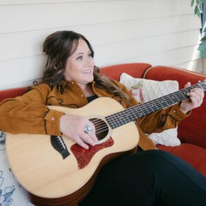 Tracy Millar photo holding guitar sitting on couch