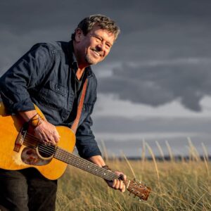 Lennie Gallant posing with guitar in the prairies with cloudy skies