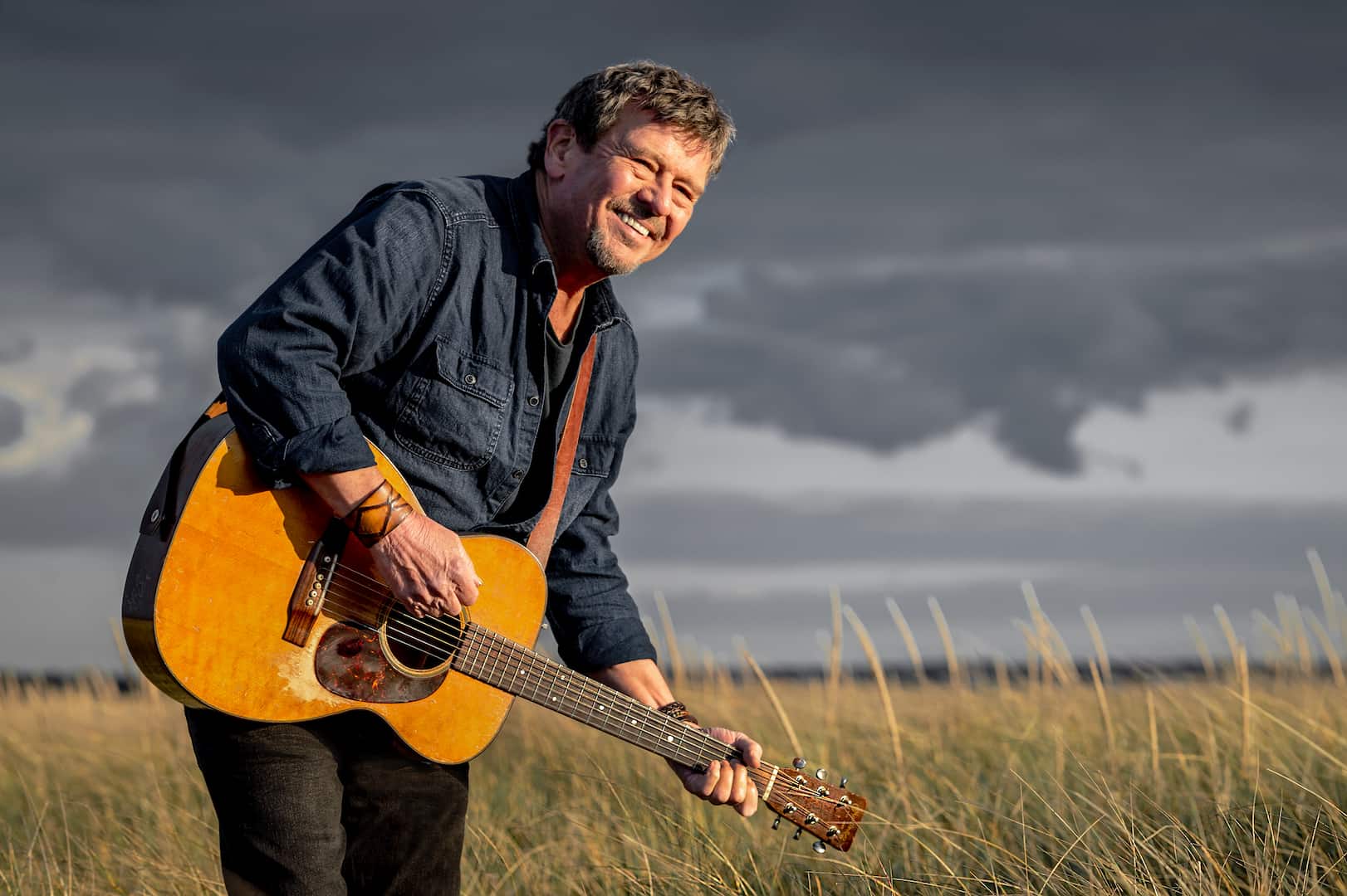 Lennie Gallant posing with guitar in the prairies with cloudy skies